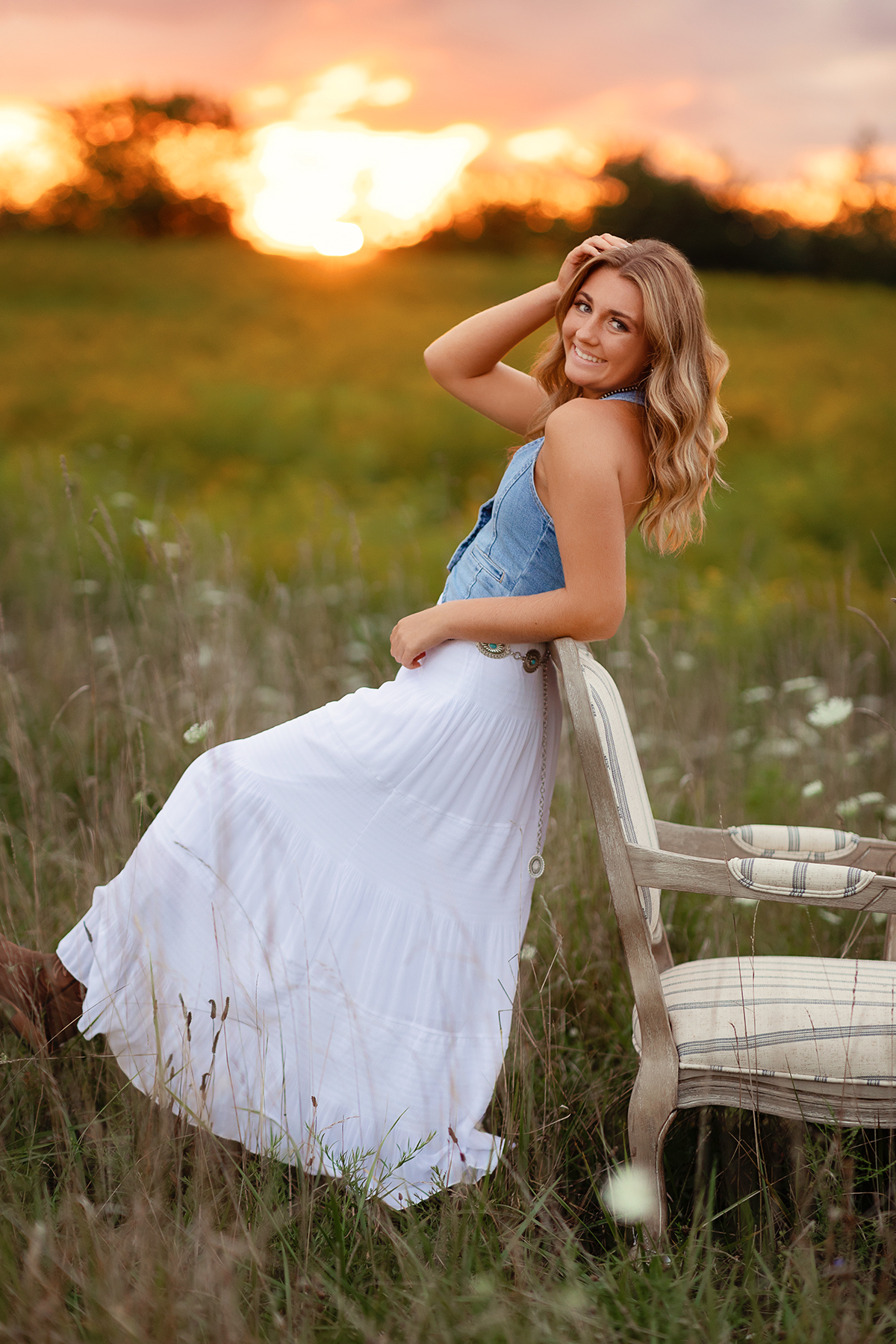 girl in white skirt in a flower field leaning against a chair